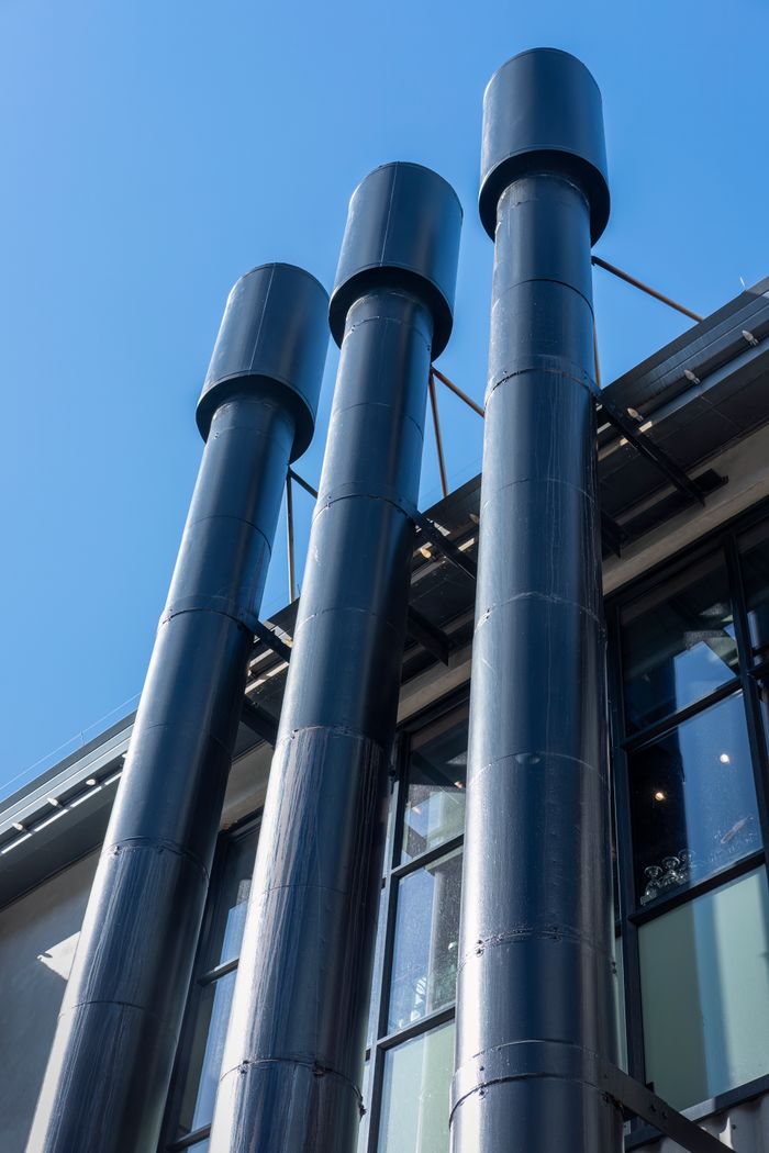 Vertical view of black industrial chimneys contrasting with a clear blue sky.